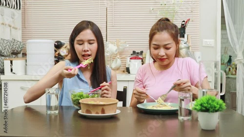 Daily life of two young Asian women who live together in a house : Delicious dinner sitting together on a salad and spaghetti dinner on the kitchen table : Relationship of best friends and take care. photo