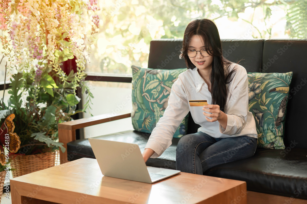 Happy young Asian woman holding credit card and using laptop for electronic payment in internet online remote store with morning sunlight. Happy young Asian woman holding credit card and using laptop for electronic payment in internet online remote store with morning sunlight.
