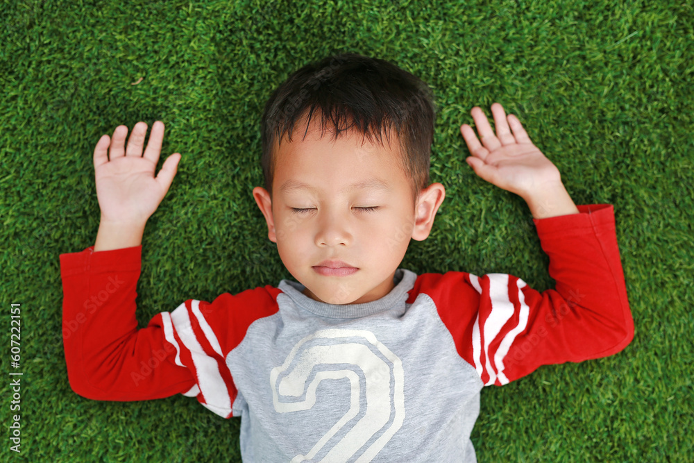 Peaceful Asian little boy close eyes and lying down on green lawn. Kid lies on grass. Top View. Peaceful Asian little boy close eyes and lying down on green lawn. Kid lies on grass. Top View.