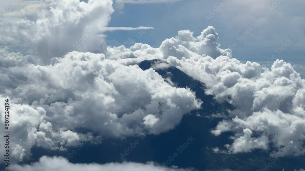 Aerial shot flying around Mount Agung volcano on the island of Bali, Indonesia, that is peaking out from a blue sky clouds on a summer day Aerial shot flying around Mount Agung volcano on the island of Bali, Indonesia, that is peaking out from a blue sky clouds on a summer day