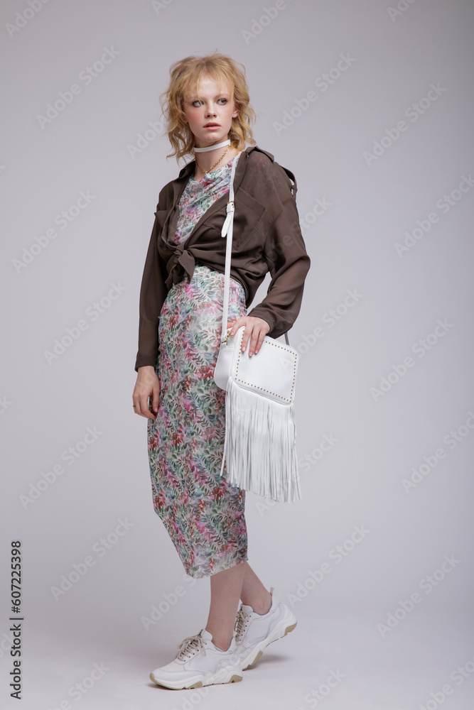 High fashion photo of beautiful elegant young woman in a pretty dress with floral pattern, green brown cardigan, choker, handbag posing over white background. Studio Shot, portrait. Blonde High fashion photo of beautiful elegant young woman in a pretty dress with floral pattern, green brown cardigan, choker, handbag posing over white background. Studio Shot, portrait. Blonde