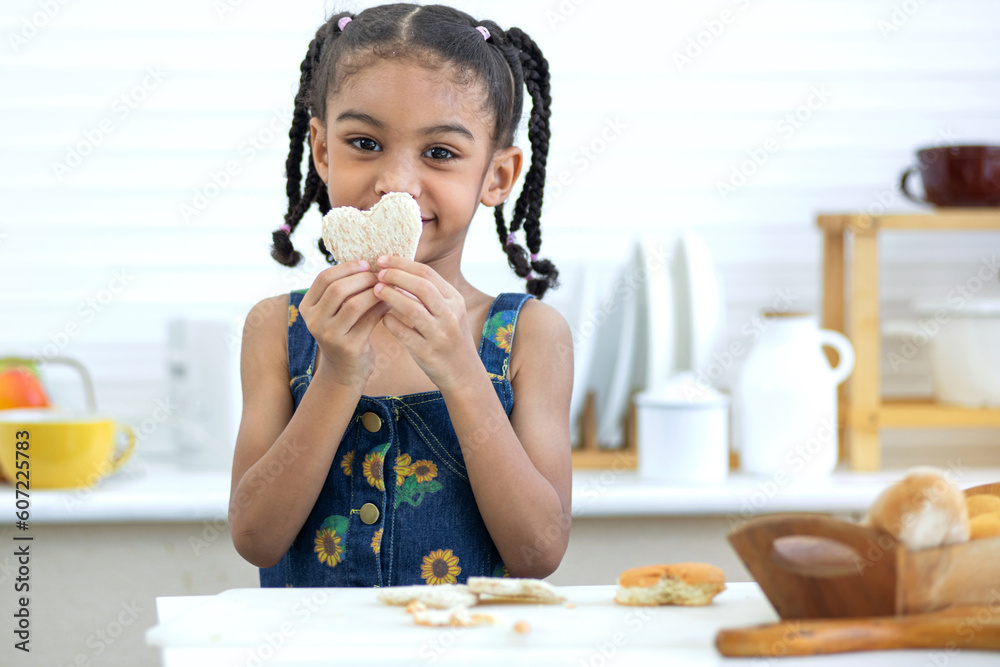 Cute little girl showing heart-shaped bread in hand at kitchen Cute little girl showing heart-shaped bread in hand at kitchen