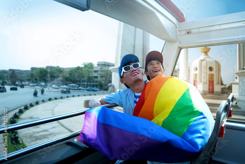 Photography LGBTQ couple with rainbow flag and hugging happily travelers on bus tour at Bang
