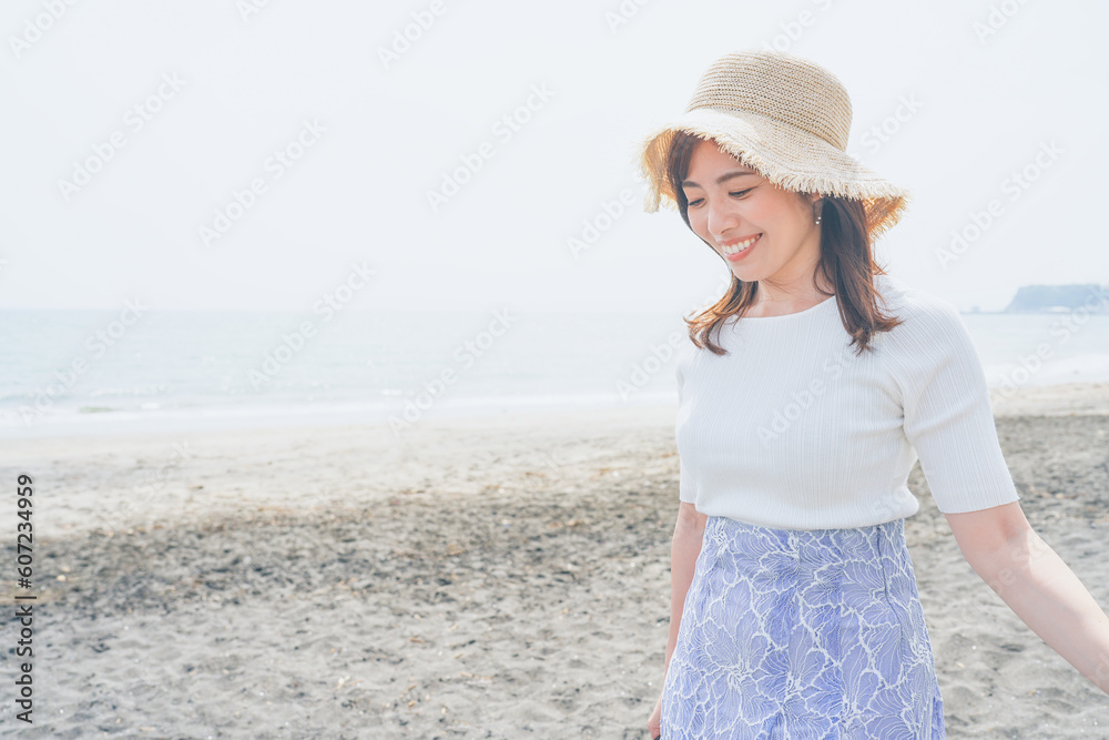 潮風を感じながら砂浜を歩く麦わら帽子の女性