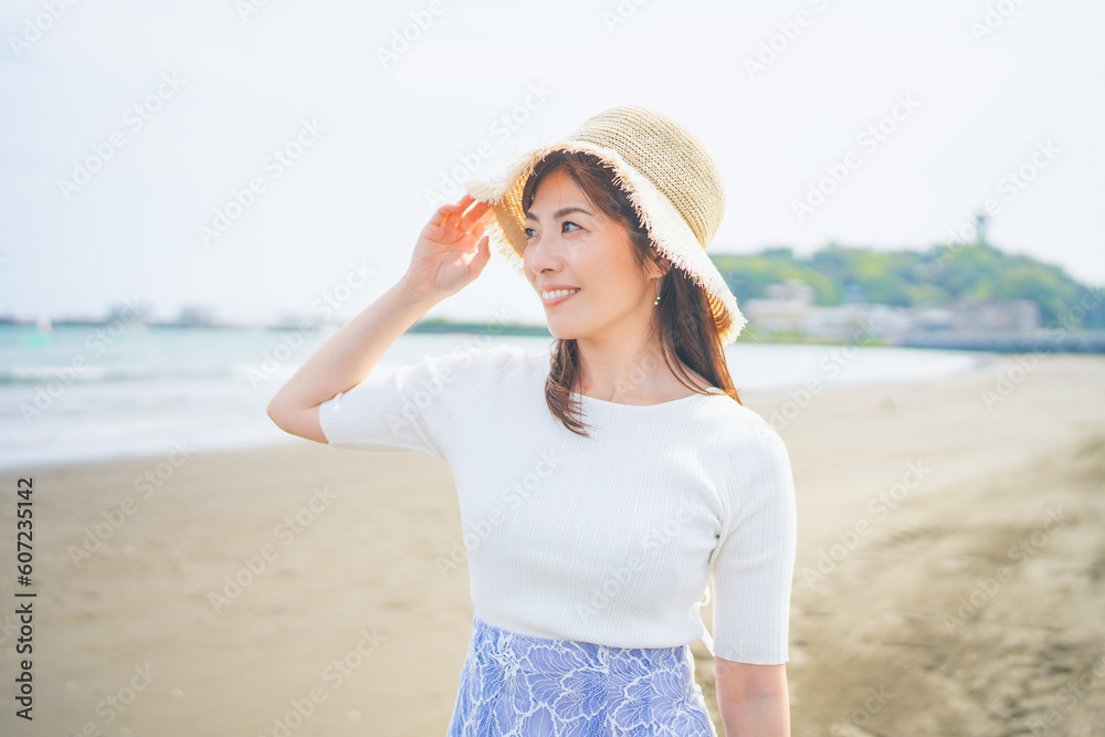 潮風を感じながら砂浜を歩く麦わら帽子の女性 潮風を感じながら砂浜を歩く麦わら帽子の女性
