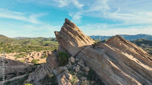 Aerial shot that wraps around the iconic Vazquez rocks which jut out of the earth at a 45 degree angle giving an magnificent otherworldly terrain that is often used for filming with green hills behind photo