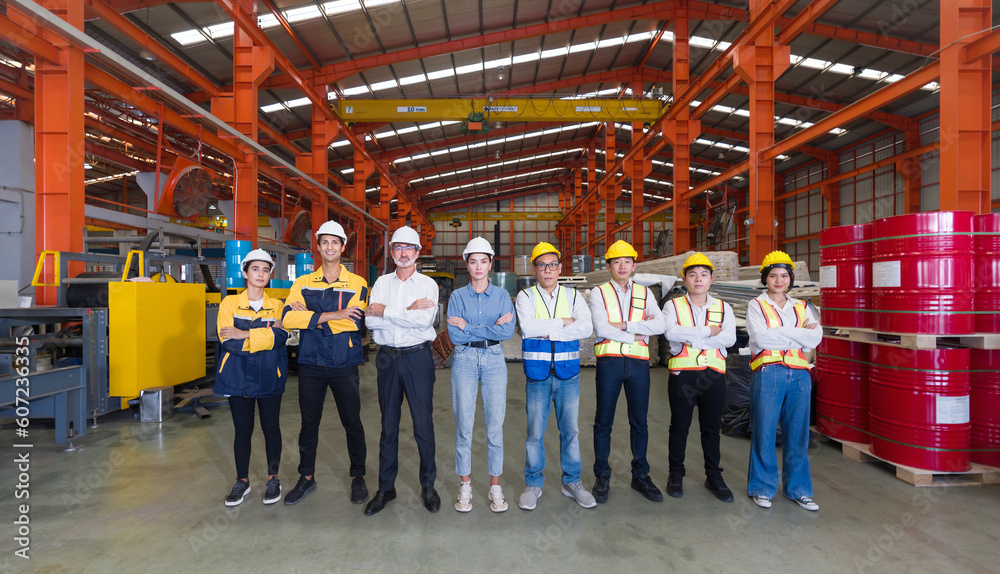 Group of male and female factory labor stand smiling together with arms crossed in industry factory. Everyone wearing safety uniform and helmet. Workers working in the metal sheet factory.