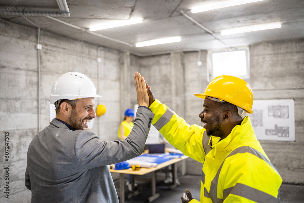 Construction worker and structural engineer giving a high five after successfully completing building project. - obrazy, fototapety, plakaty 