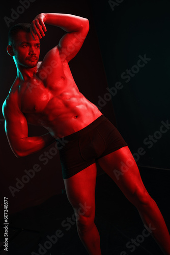 Man bodybuilder athlete with bare torso fashion pose on black isolated background with colored light neon red and green. The concept of a healthy male body sport