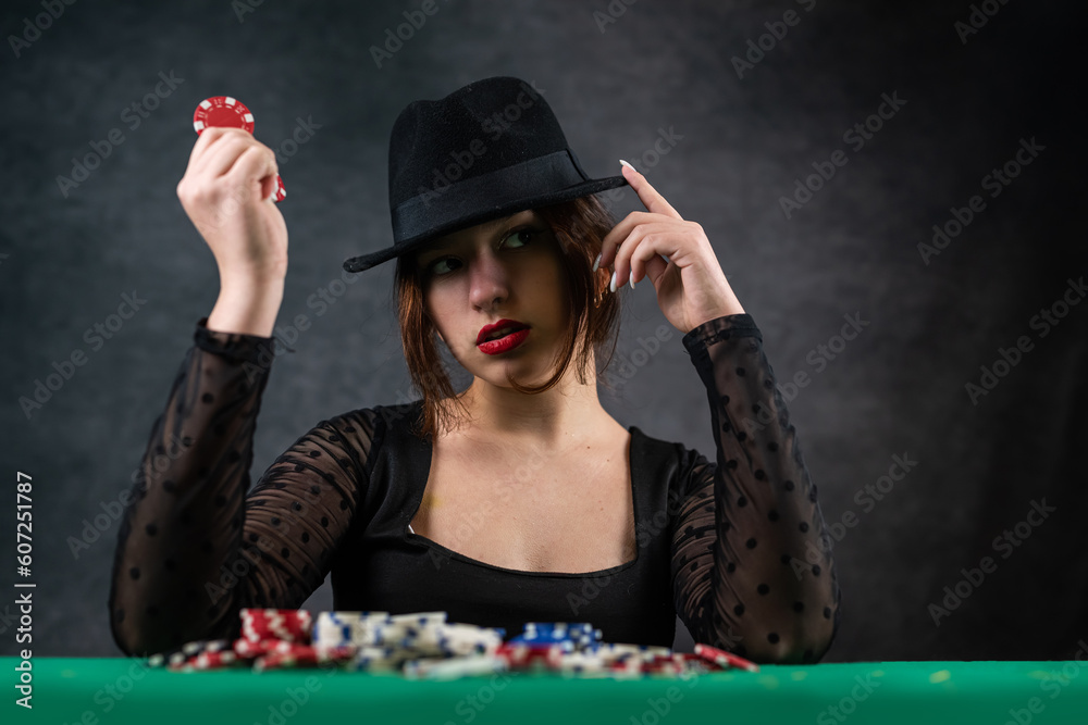 attractive girl in a black dress is leaning on the table, holding a poker chip and looking away. poker. casino attractive girl in a black dress is leaning on the table, holding a poker chip and looking away. poker. casino