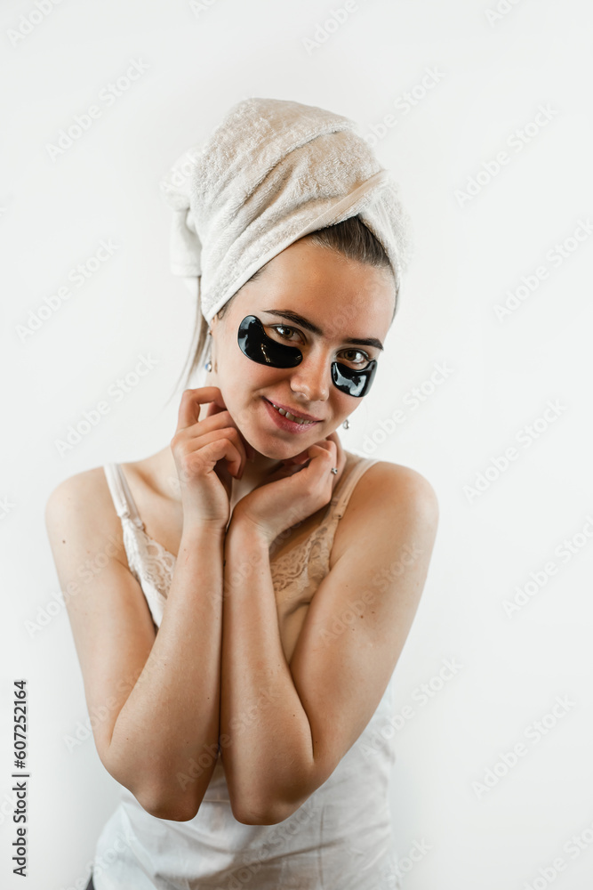 Pretty young lady in white towel applying collagen hydrogel patches under the eyes to smooth the skin isolated on white Pretty young lady in white towel applying collagen hydrogel patches under the eyes to smooth the skin isolated on white