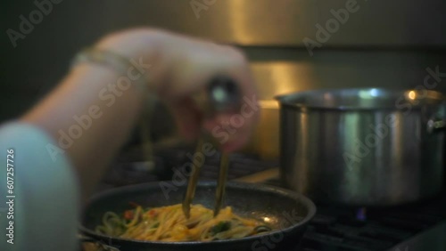 Vegetable pasta stirred and flipped in hot frying pan on kitchen stove, filmed as close up photo