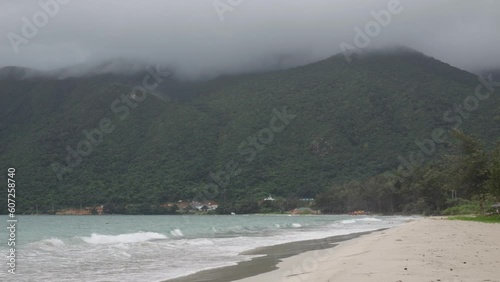 Slow-motion shot of Bãi tắm An Hải Beach, Con Dao Island, Vietnam. Waves crashing on sandy beach, mist-covered mountains in the background. Serene coastal beauty in a captivating scene photo