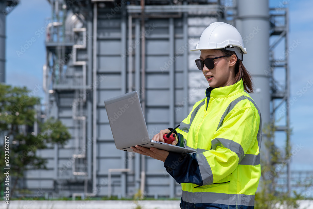 Engineer wearing uniform ,helmet and glass stand hand holding tablet computer,radio communication inspection and surveying work site progress with oil refinery power industrial factory background