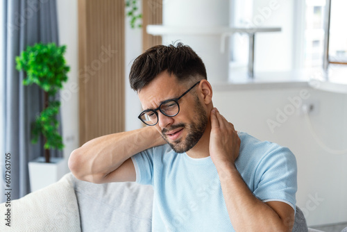 Unhappy young man suffering from pain in the neckache , exhausted unwell man having nech overwhelmed with work. Health problem concept photo