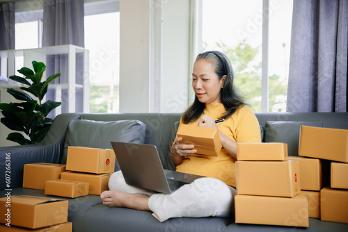 Mature business owner woman prepare parcel box and standing check online orders for deliver to customer on tablet, laptop Shopping Online © laddawan