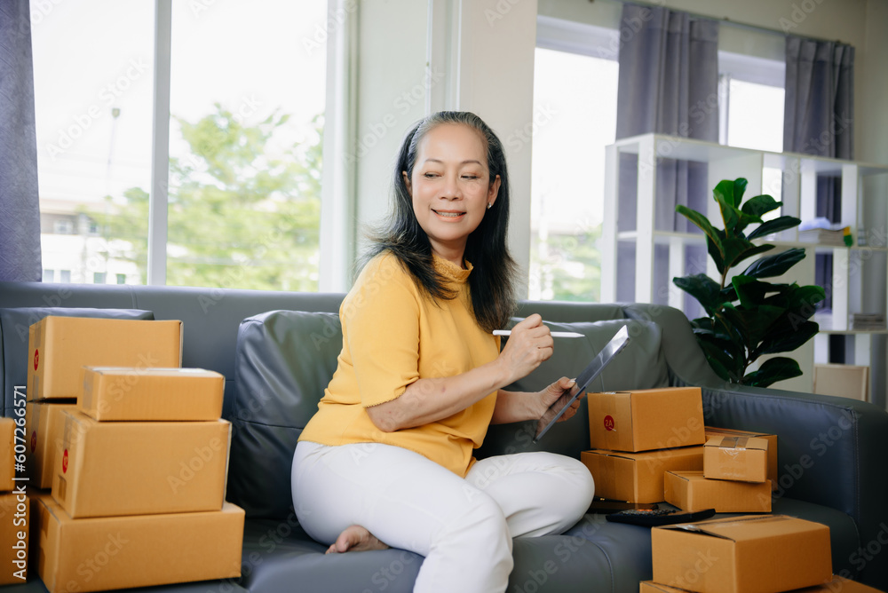 Mature business owner woman prepare parcel box and standing check online orders for deliver to customer on tablet, laptop Shopping Online Mature business owner woman prepare parcel box and standing check online orders for deliver to customer on tablet, laptop Shopping Online