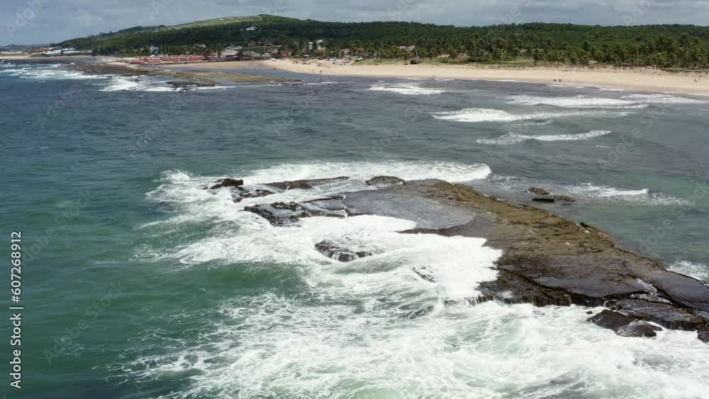 Rotating aerial drone shot of small waves crashing into a long rock during high tide on the famous tropical Sibauma beach creating natural ocean pools for swimming in Rio Grande do Norte, Brazil Rotating aerial drone shot of small waves crashing into a long rock during high tide on the famous tropical Sibauma beach creating natural ocean pools for swimming in Rio Grande do Norte, Brazil