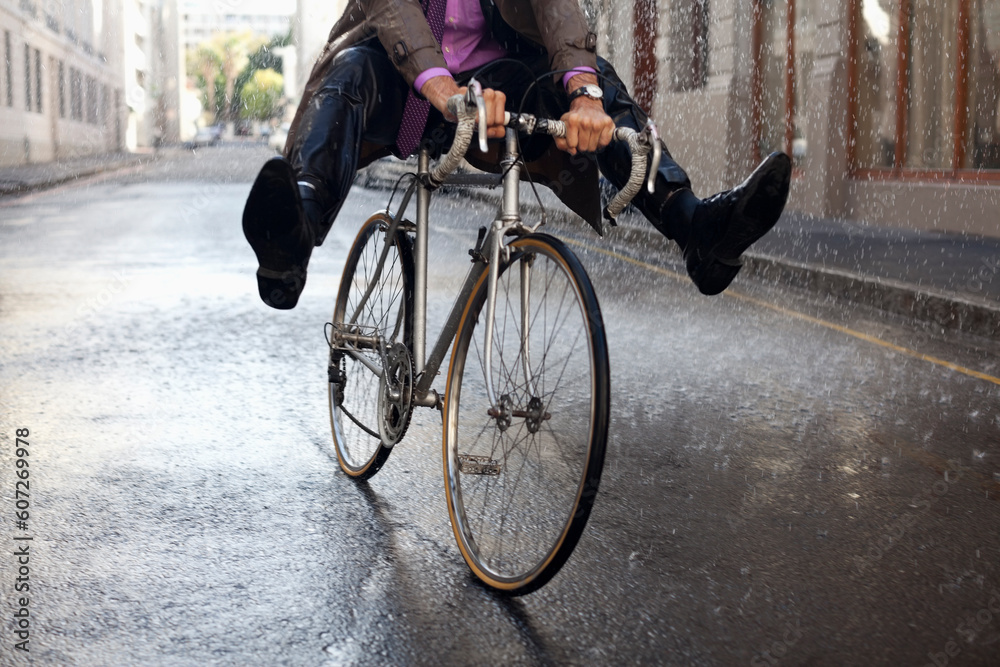Businessman riding bicycle with feet up in rain