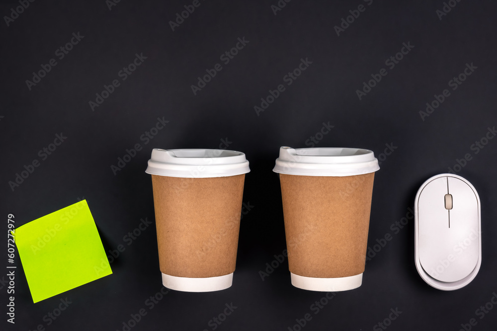 Paper cups, computer mouse and paper sticker on a dark background, top view. Paper cups, computer mouse and paper sticker on a dark background, top view.