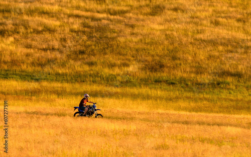 Man riding cross motorcycle dirt bike through Zlatibor grassy landscape on sunny summer day