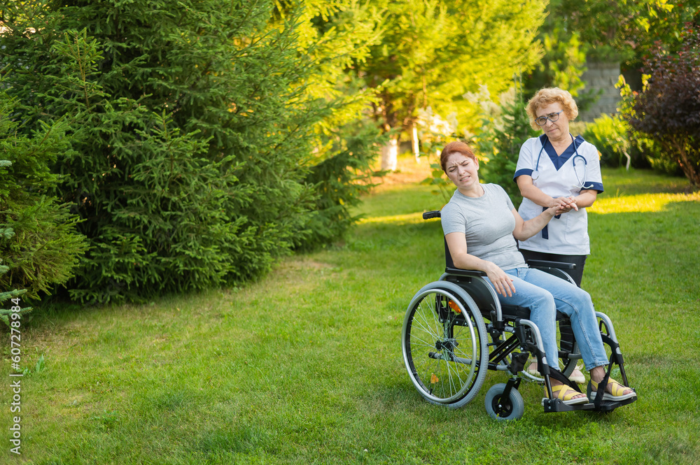 Elderly nurse comforting woman sitting in wheelchair outdoors. Elderly nurse comforting woman sitting in wheelchair outdoors.