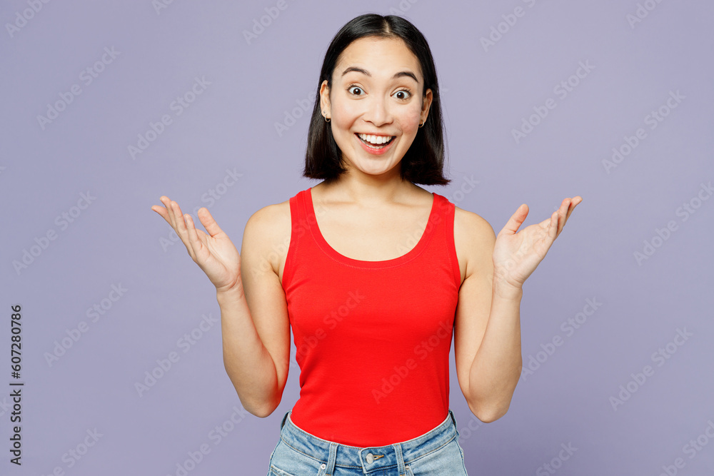 Young fun surprised shocked excited woman of Asian ethnicity she wear casual clothes red tank shirt spead hands look camera isolated on plain pastel light purple background studio. Lifestyle concept. Young fun surprised shocked excited woman of Asian ethnicity she wear casual clothes red tank shirt spead hands look camera isolated on plain pastel light purple background studio. Lifestyle concept.