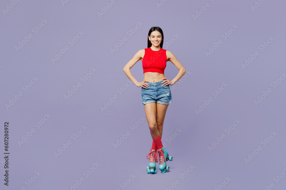 Full body happy smiling young latin woman she wear red casual clothes rollers stand akimbo hands on waist look camera isolated on plain pastel purple background Summer sport lifestyle leisure concept