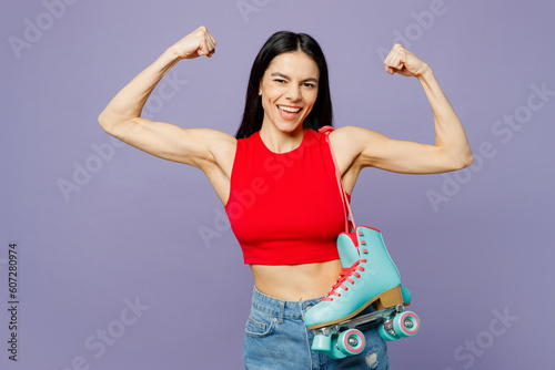 Young sporty latin woman she wear red casual clothes hold rollers show biceps muscles on hand demonstrating strength power isolated on plain pastel purple background. Summer lifestyle leisure concept.