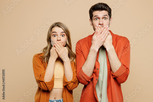 Young shocked sad surprised couple two friends family man woman wear casual clothes cover mouth with hand looking camera together isolated on pastel plain light beige color background studio portrait.