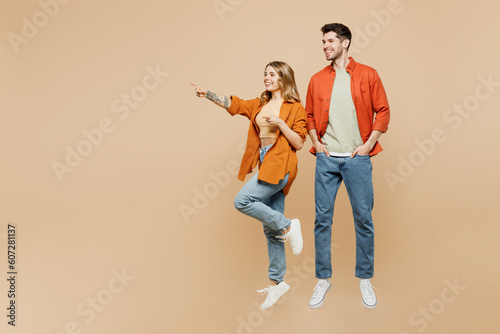 Full body fun young couple two friends family man woman wearing casual clothes together point index finger aside on area mock up isolated on pastel plain light beige color background studio portrait.