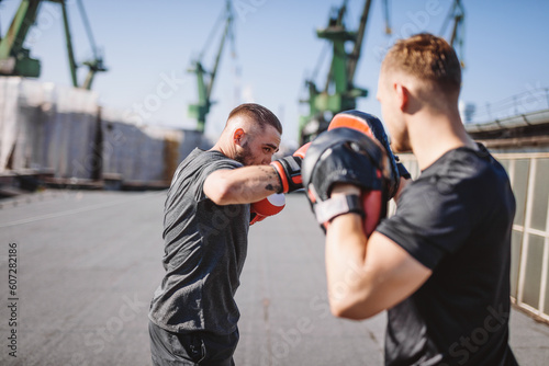 Two men do boxing training on roof of the building in industrial city