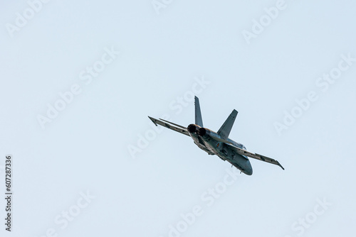 Rear view of a hornet F-18 jet fighter in an Air show festival flying at sub-sonic speed in a clear blue sky with no ammo installed for the exhibition