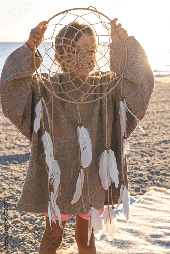 Little girl with a dream catcher on the seashore at sunset.