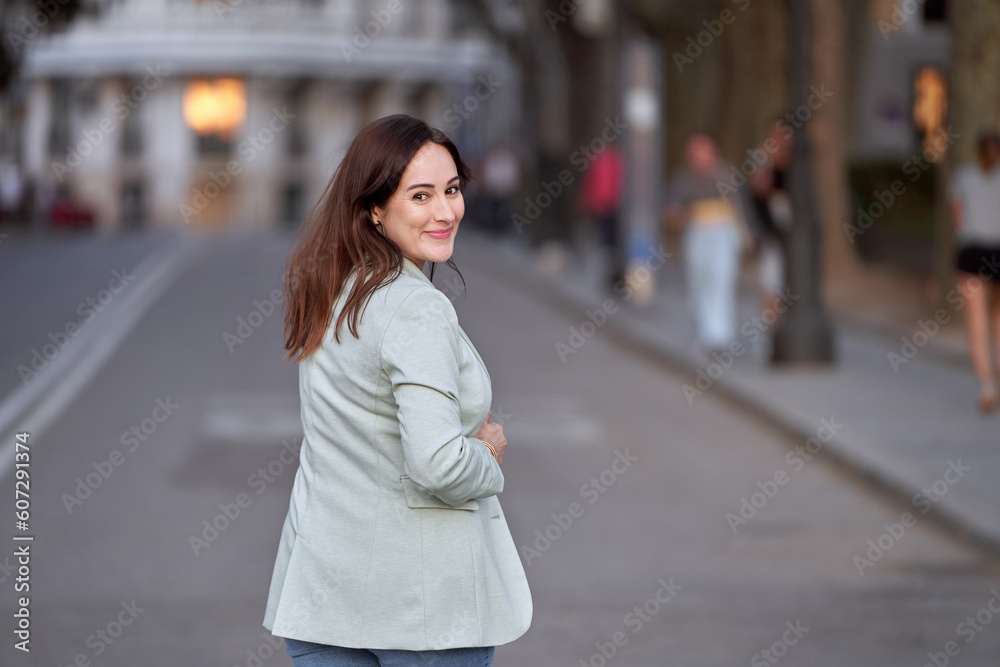 Woman looking back to camera and smiling while walking outdoors on the street. Woman looking back to camera and smiling while walking outdoors on the street.