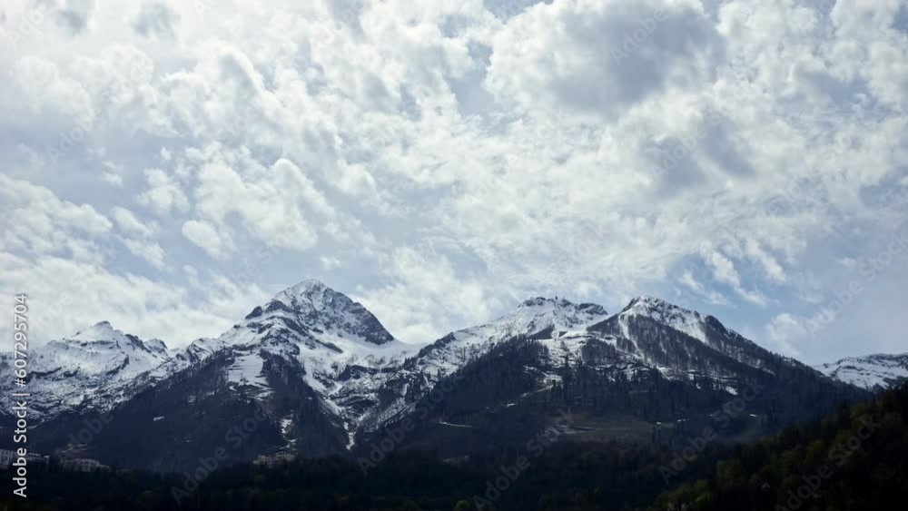White clouds in blue sky moving over snowy white mountains during sunny day. Bright sunlight illuminates hills and slopes of highland time lapse White clouds in blue sky moving over snowy white mountains during sunny day. Bright sunlight illuminates hills and slopes of highland time lapse