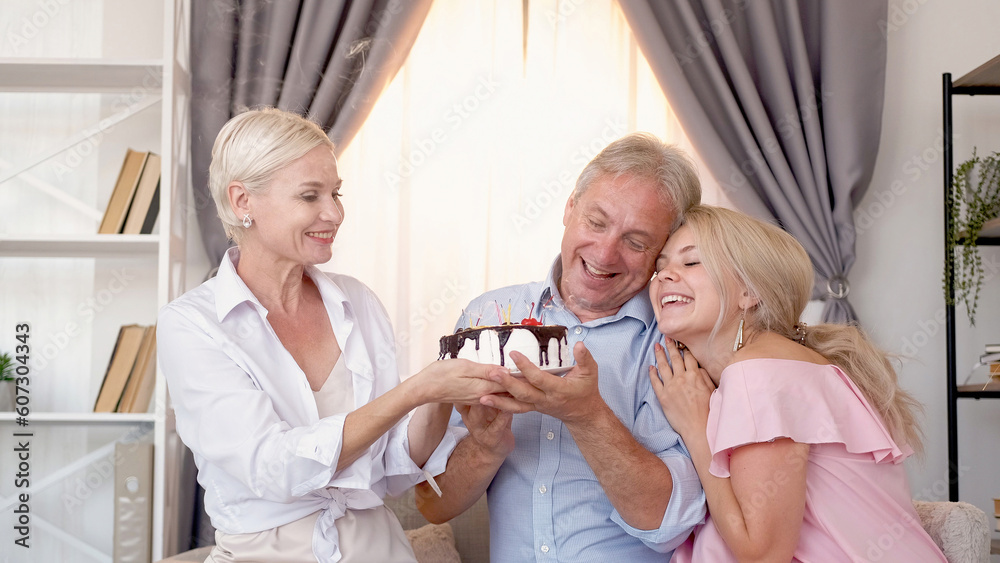 Birthday greeting. Family celebration. Holiday cake. Excited man woman and daughter holding festive pastry in light home interior. Birthday greeting. Family celebration. Holiday cake. Excited man woman and daughter holding festive pastry in light home interior.