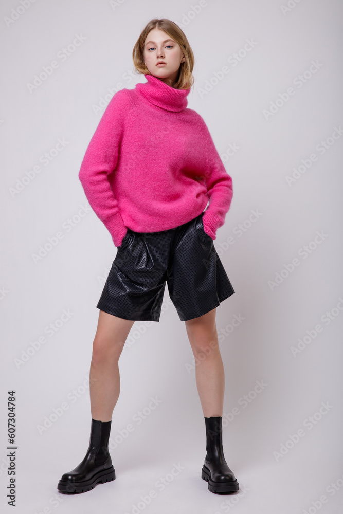 Fashion photo of a beautiful elegant young woman in a pretty pink fuchsia sweater, blouse, black leather shorts posing on white, soft gray background. Studio Shot, portrait. Slim figure. Blonde Fashion photo of a beautiful elegant young woman in a pretty pink fuchsia sweater, blouse, black leather shorts posing on white, soft gray background. Studio Shot, portrait. Slim figure. Blonde
