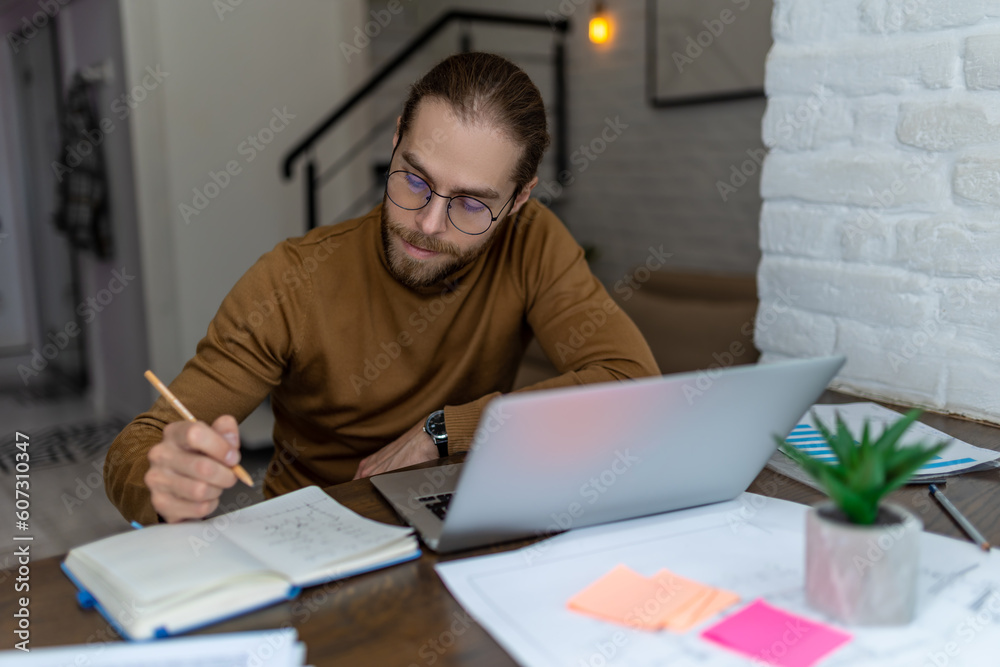Man using laptop writing down important data in notebook, working on computer or studying online. Man using laptop writing down important data in notebook, working on computer or studying online.