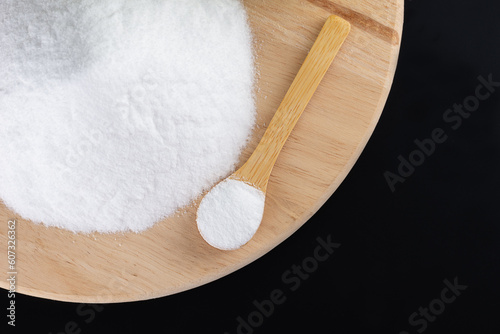 Pile of glucose or grape sugar in a spoon on a wooden board, black background.