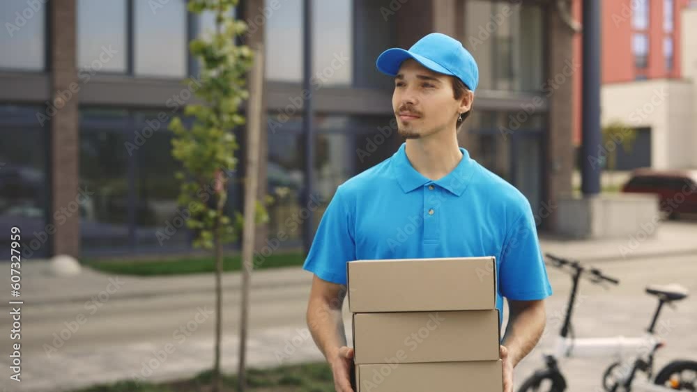 Smiling Positive Caucasian Postman Holding the Paper Boxes. Walking Outside. Male Delivery Wearing Special Uniforms Carrying the Boxes. People and Professions. Delivering Service Smiling Positive Caucasian Postman Holding the Paper Boxes. Walking Outside. Male Delivery Wearing Special Uniforms Carrying the Boxes. People and Professions. Delivering Service