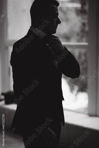 Silhouette of stylish groom stand in front of big window. Groom's morning