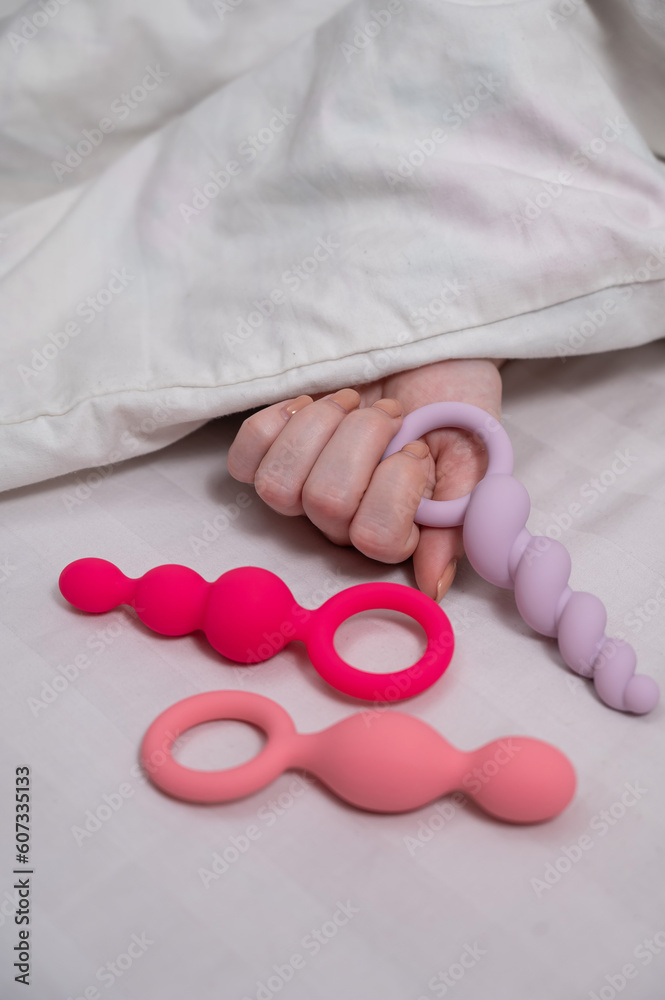 A woman chooses anal beads from a set while lying in bed. Stock Photo |  Adobe Stock