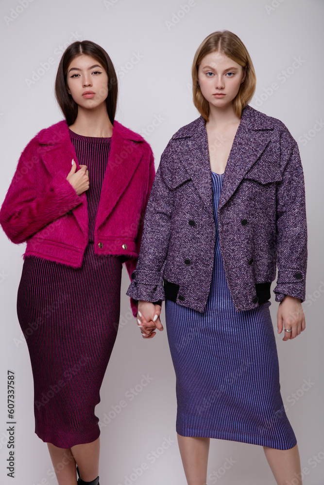 Two fashion models in pink fuchsia and blue dress, jacket. Beautiful young woman. Studio shot, portrait. White background. Asian and blonde. Slim figure Two fashion models in pink fuchsia and blue dress, jacket. Beautiful young woman. Studio shot, portrait. White background. Asian and blonde. Slim figure