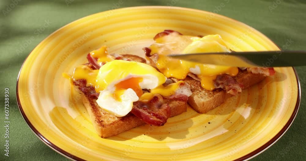 Cutting Benedict eggs on a plate. Serving breakfast on a colored background. Boiled eggs on bread with fried bacon and hollandaise sauce. Angle view. Smooth camera movement. Zoom. Sunny day. Cutting Benedict eggs on a plate. Serving breakfast on a colored background. Boiled eggs on bread with fried bacon and hollandaise sauce. Angle view. Smooth camera movement. Zoom. Sunny day.