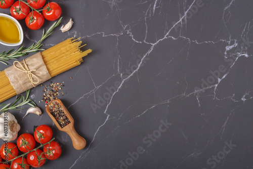 Ingredients for italian pasta. Spaghetti, tomatoes, olive oil, garlic and rosemary on dark gray marble kitchen table . Top view. Copy space

