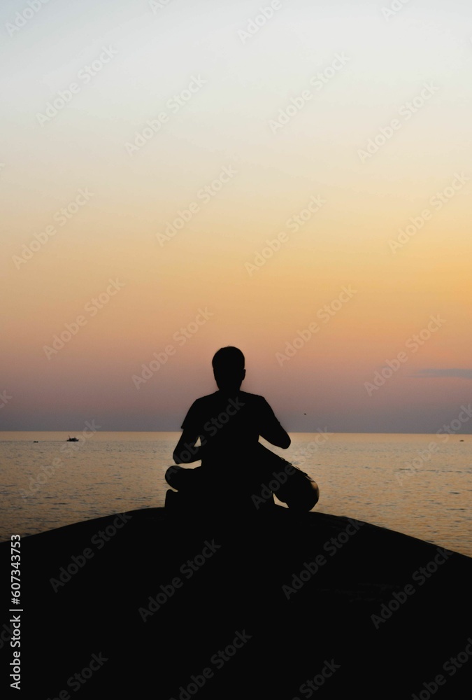 Vertical shot of a silhouette of a person meditating on the seashore at sunset