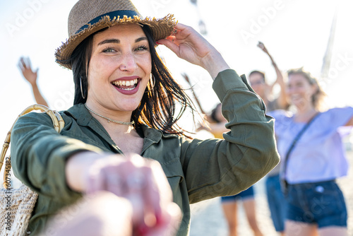 Young brunette woman with blue eyes inviting you to dance in a beach party, musical international festival with happy crowd of people