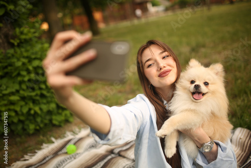 Caucasian girl student female pet owner taking selfie photo with dog, image on smart phone, having video call conversation with dog online in park