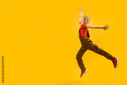 Side view full-length portrait of bouncing boy on yellow background. Child jumps happily. Copy space, place for text © somemeans
